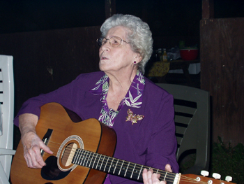 An elderly woman playing guitar and singing