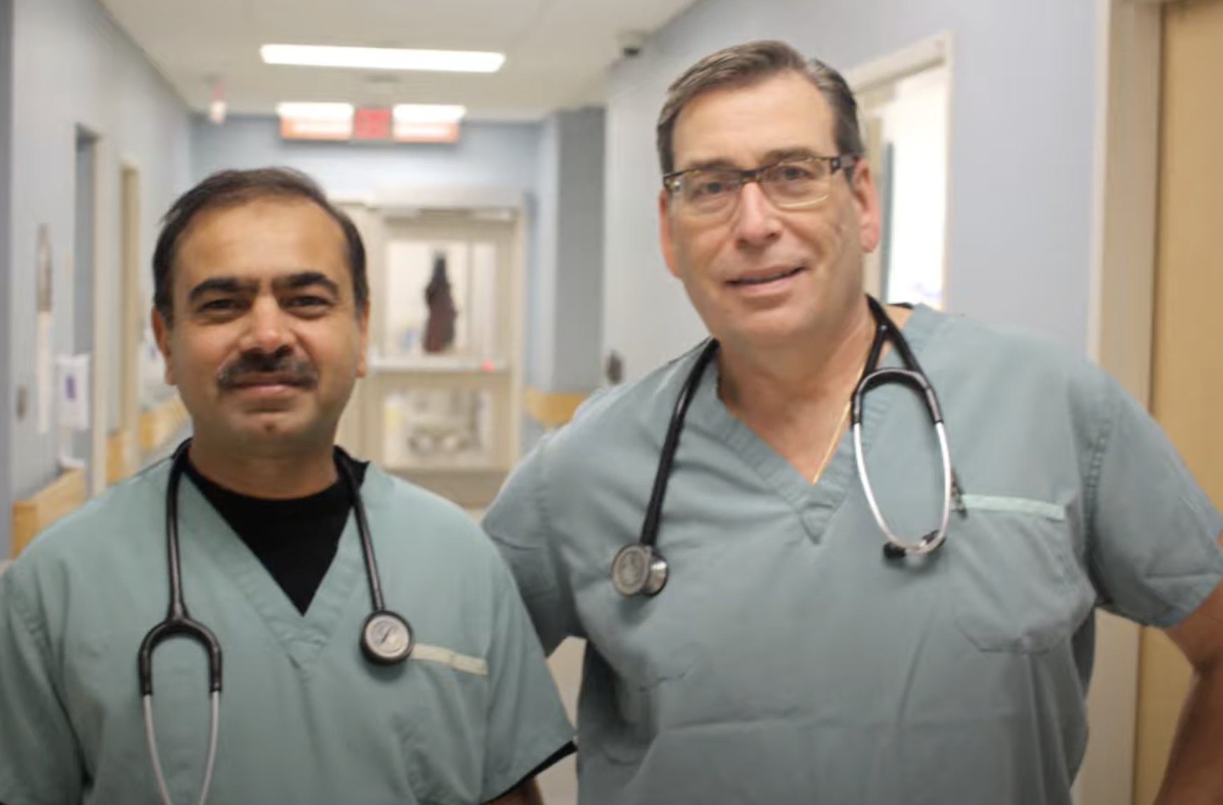 Two male doctors wearing scrubs in a hospital hallway